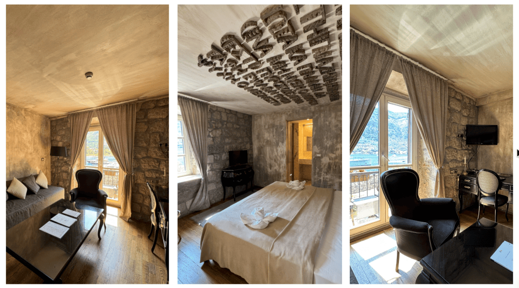 A beautifully designed hotel room featuring stone walls, large windows with drapes, and modern furnishings including a sofa, chairs, and a desk.